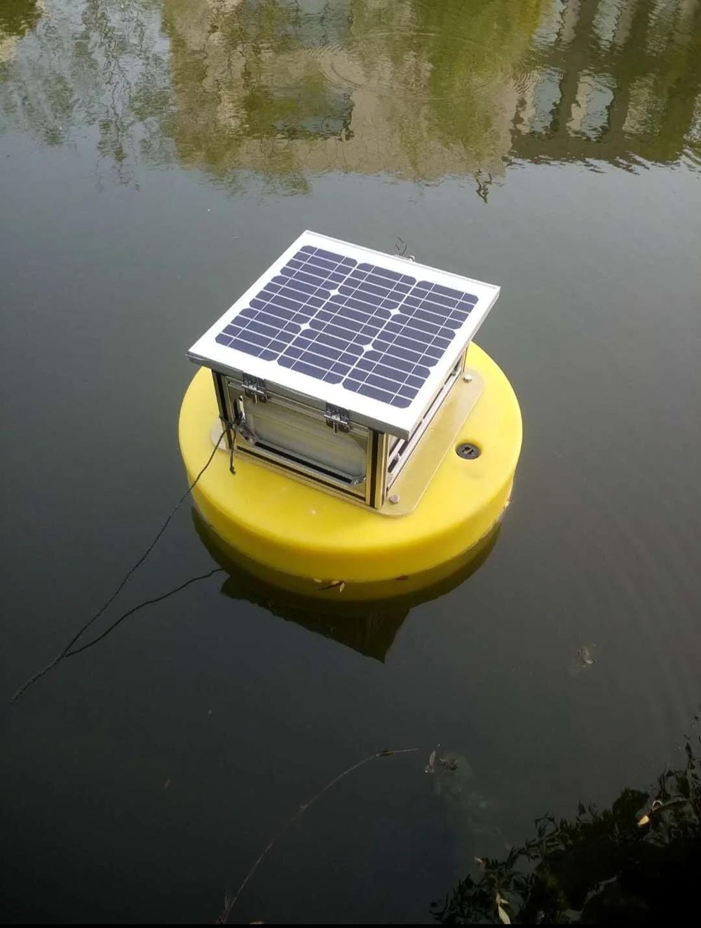 Yellow floating sensor buoy with a solar panel on top, floating on pond water